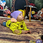 Asher joined the competition — help win amazing prizes! toddler, child, costume, purple_hat, yellow_clothing, lying_down, face, hands, wood_pattern, blanket, mushrooms, toy_bird, pickaxe, background, indoor, playful, portrait, curious, props, colorful