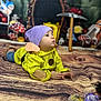toddler, child, costume, purple_hat, yellow_clothing, lying_down, face, hands, wood_pattern, blanket, mushrooms, toy_bird, pickaxe, background, indoor, playful, portrait, curious, props, colorful