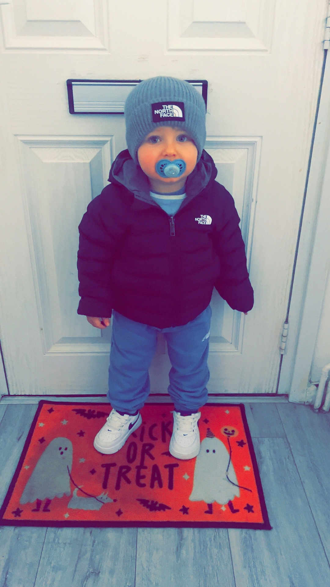 Luca joined the competition — help win amazing prizes! child, baby, pacifier, hat, jacket, sneakers, door, doormat, floor, indoor, clothing, standing, north_face, blue_pants, white_shoes, halloween, ghosts, trick_or_treat, cute, winter_wear