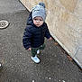 Aaron participe au concours pour gagner de l'argent avec cette photo : toddler, child, pavement, jacket, beanie, hat, pom_pom, sloth_pattern, white_shoes, sidewalk, wall, outdoor, winter_clothing, curious_expression, standing, small_person, urban, cold_weather, casual, person
