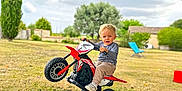 Gabriel participe au concours pour gagner de l'argent avec cette photo : blonde_hair, casual_clothing, chair, child, cloudy, daytime, fun, grass, greenery, house, nature, outdoor, play, rural, sky, toddler, toy_motorcycle, tree, wheelie, young_child