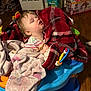 Rosie is registered to the contest to win money with this photo: baby, blanket, child, sleeping, toy, indoor, activity_seat, face, furniture, floor, wooden_floor, plaid_blanket, clothing, head, person, pacifier, box, household, infant, rest