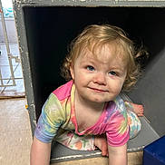 Rosie joined the competition — help win amazing prizes! toddler, child, crawling, curly_hair, smiling, indoor, colorful_clothing, tie_dye, floral_pants, cubbyhole, floor, playful, blue_wall, carpet, barefoot, light_skin, young_child, happy, cute, portrait