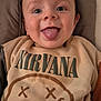 baby, child, tongue_out, smiling, face, sweatshirt, nirvana, clothing, baby_seat, cushion, toy_rings, happy, indoor, cute, infant, person, portrait, young_child, cozy, casual