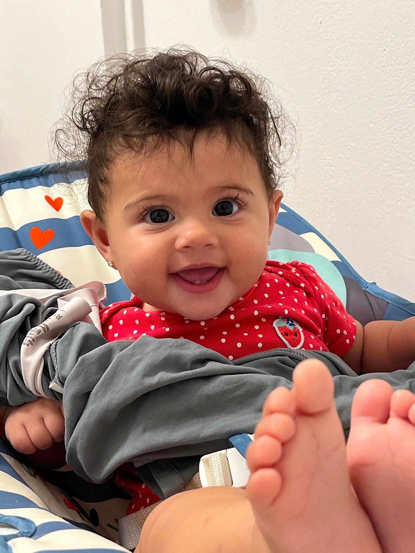 Maylani joined the competition — help win amazing prizes! baby, smiling, curly_hair, red_clothing, polka_dots, baby_seat, heart_pattern, barefoot, face, eyes, hands, blanket, indoor, cute, happy, child, infant, person, earrings, portrait