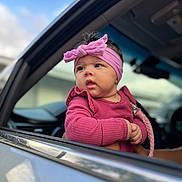 Maylani joined the competition — help win amazing prizes! baby, child, pink_headband, pink_clothing, car_window, car_interior, curious_expression, infant, outdoor, portrait, cute, hands, face, headwear, person, window_frame, vehicle, young_child, soft_light, closeup