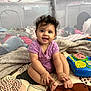 baby, child, smiling, curly_hair, purple_onesie, sitting, toys, blanket, quilt, indoor, play_area, cute, hands, feet, face, happy, infant, colorful, playtime, home
