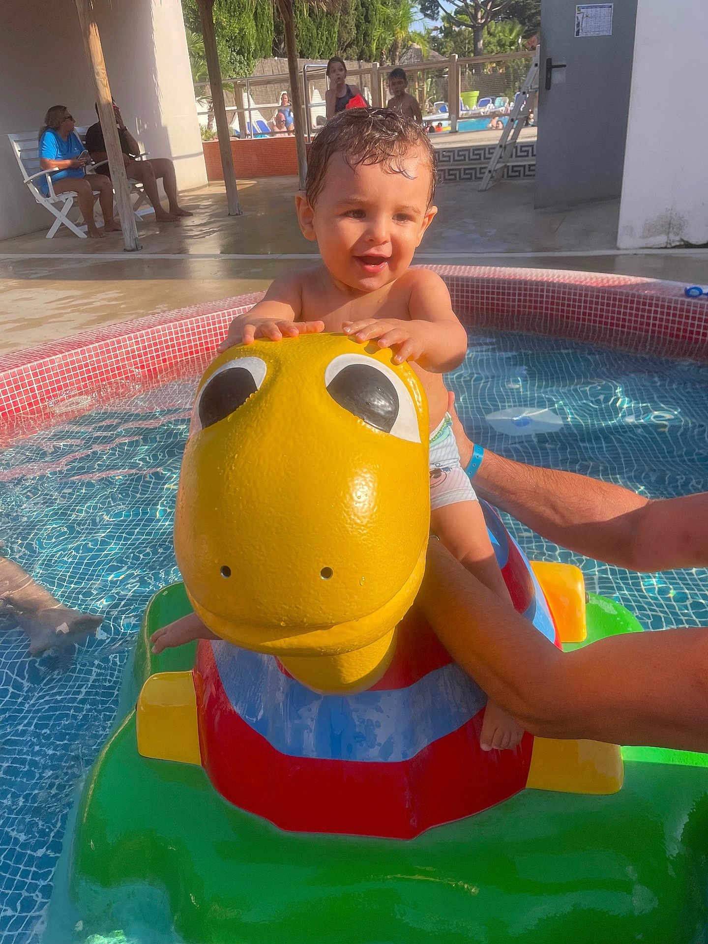Ilyan participe au concours pour gagner de l'argent avec cette photo : adult_arm, child, dinosaur, family, float, fun, happy, outdoor, people, play, pool, summer, sunlight, swimming_pool, toddler, toy, vacation, water, water_toy, yellow