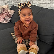 Ckaÿnni a rejoint le concours — aidez-le/la à gagner de superbes lots ! baby, child, smiling, couch, indoor, headband, bow, brown_sweater, plaid_skirt, boots, drool, pillow, brick_wall, happy, person, sitting, cute, cozy, home, infant