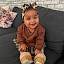 baby, child, smiling, couch, indoor, headband, bow, brown_sweater, plaid_skirt, boots, drool, pillow, brick_wall, happy, person, sitting, cute, cozy, home, infant