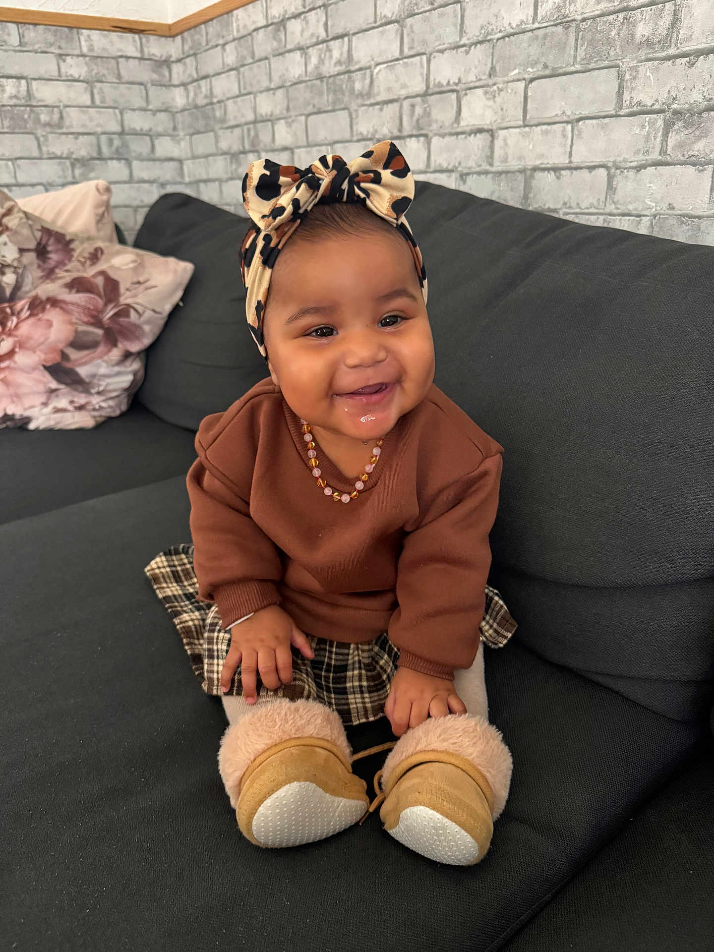 Ckaÿnni a rejoint le concours — aidez-le/la à gagner de superbes lots ! baby, child, smiling, couch, indoor, headband, bow, brown_sweater, plaid_skirt, boots, drool, pillow, brick_wall, happy, person, sitting, cute, cozy, home, infant