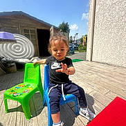 Elyo participe au concours pour gagner de l'argent avec cette photo : blue_chair, building, casual, child, clothing, concrete_floor, daylight, fence, green_chair, nike, outdoor, pants, person, plastic_chair, shed, sky, sneakers, sunlight, trees, tshirt