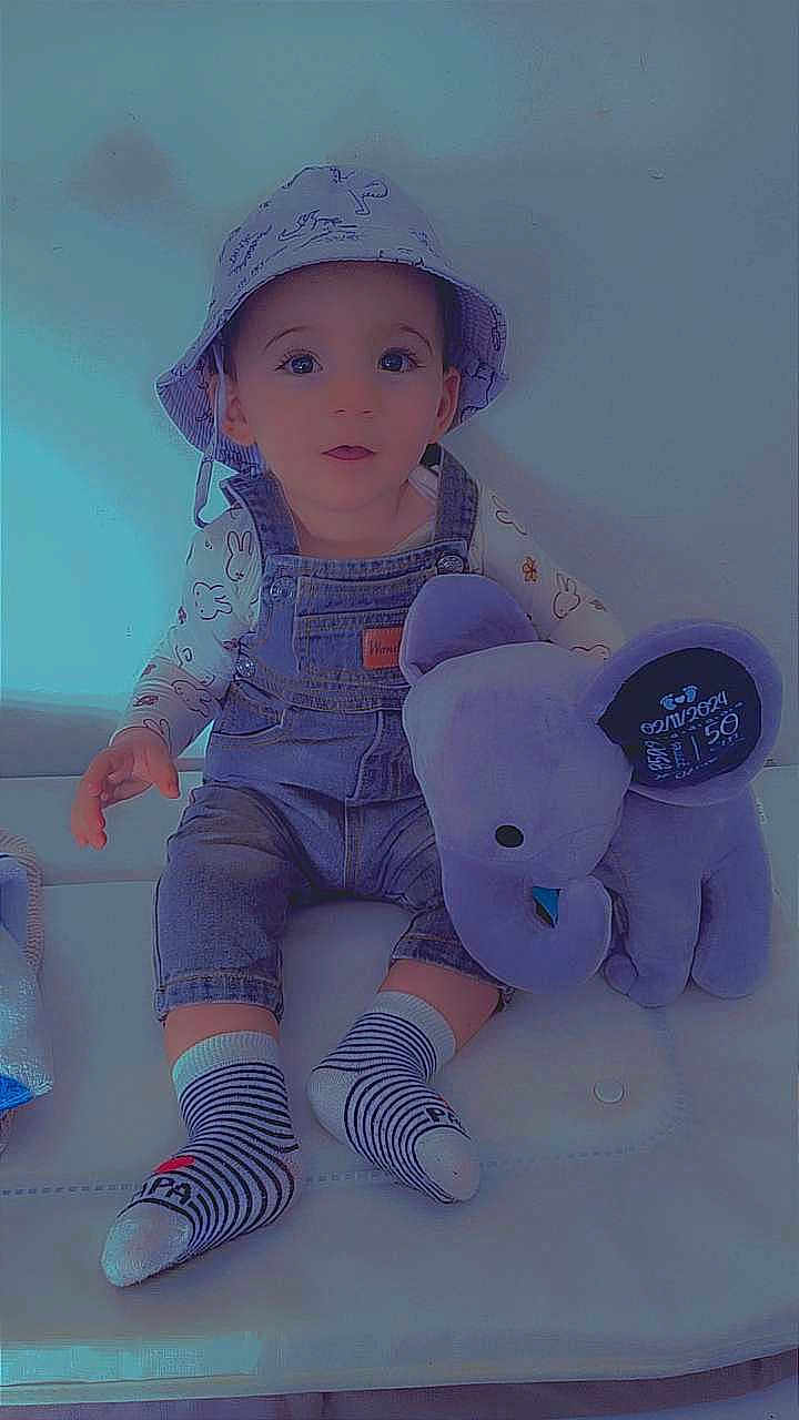 Kezio a rejoint le concours — aidez-le/la à gagner de superbes lots ! toddler, child, hat, bucket_hat, denim_overalls, plush_toy, elephant, purple, striped_socks, sitting, indoors, cute, baby_clothes, childrens_fashion, smiling, young_child, face, person, cushion, white_background