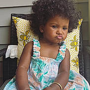 Ryver joined the competition — help win amazing prizes! toddler, child, afro_hair, curly_hair, pouty_face, dress, patterned_dress, chair, pillow, yellow_pillow, indoor, cute, baby, hands, feet, skin, earrings, bracelet, expression, portrait