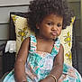 toddler, child, afro_hair, curly_hair, pouty_face, dress, patterned_dress, chair, pillow, yellow_pillow, indoor, cute, baby, hands, feet, skin, earrings, bracelet, expression, portrait