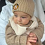 baby, child, beanie, knitwear, mickey_mouse, hat, hands, face, blue_eyes, hoodie, white_clothing, person, closeup, portrait, warm_clothing, cute, indoor, holding, sweater, button