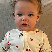 Celeste is registered to the contest to win money with this photo: toddler, child, onesie, cherry_pattern, earrings, sitting, blanket, indoor, cute, portrait, face, hair, clothing, young_child, baby, expression, person, infant, cozy, casual