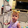 toddler, child, playpen, toy, headband, dress, indoor, living_room, television, furniture, decor, floor, baby, curious, person, face, expression, colorful, play, home