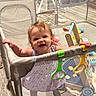 Celeste is registered to the contest to win money with this photo: toddler, child, playpen, toys, indoor, smiling, happy, baby, mesh, furniture, wood_floor, clothing, earrings, play_area, colorful, plastic, person, standing, home, cute