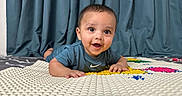 Nived is registered to the contest to win money with this photo: baby, blue, child, clothing, curtains, cute, expression, face, hands, happy, indoor, lying_down, person, play_mat, portrait, short_hair, skin, smiling, toddler, young