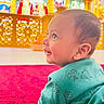baby, child, smiling, red_carpet, teal_shirt, indoor, religious_altar, golden_decor, portrait, happy, crawling, young_child, face, head, floor, bright_colors, cute, side_view, person, infant
