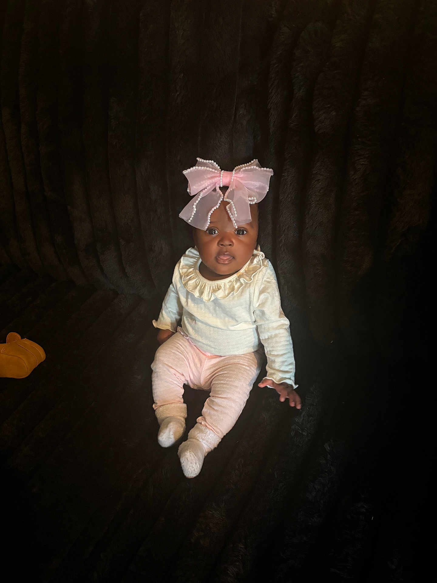 Kanova is registered to the contest to win money with this photo: baby, child, pink_bow, sitting, dark_background, plush, cozy_clothing, socks, curious_expression, indoor, footwear, portrait, infant, cute, adorable, soft_lighting, person, young_child, headwear, fashion