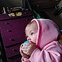 baby, child, hoodie, pink_clothing, blue_eyes, indoor, furniture, dresser, toy, hands, face, person, casual_clothing, room, curious, closeup, candid, young_child, soft_lighting, cozy