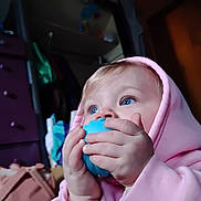 Phoebe is registered to the contest to win money with this photo: baby, child, hoodie, blue_eyes, toy, indoor, hands, face, curious, soft_lighting, closeup, infant, cute, pink_clothing, blue_toy, portrait, young_child, focus, background_blur, home