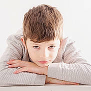 Sohann a rejoint le concours — aidez-le/la à gagner de superbes lots ! child, boy, portrait, face, brown_hair, light_skin, sweater, long_sleeves, resting, hands, looking_at_camera, white_background, minimalist, casual_clothing, indoor, young, expression, close_up, calm, serene