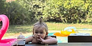 Julia a rejoint le concours — aidez-le/la à gagner de superbes lots ! toddler, child, outdoor, picnic_table, sippy_cup, cookie, pool, inflatable, flamingo_float, grass, summer, hair_tie, top_knot, table, chair, person, daytime, thinking, relaxed, backyard
