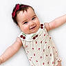 Livia is registered to the contest to win money with this photo: baby, infant, smile, chubby_cheeks, headband, red_bow, romper, cherry_pattern, cute, happy, lying_down, white_background, arms_outstretched, adorable, child, portrait, face, skin, person, young