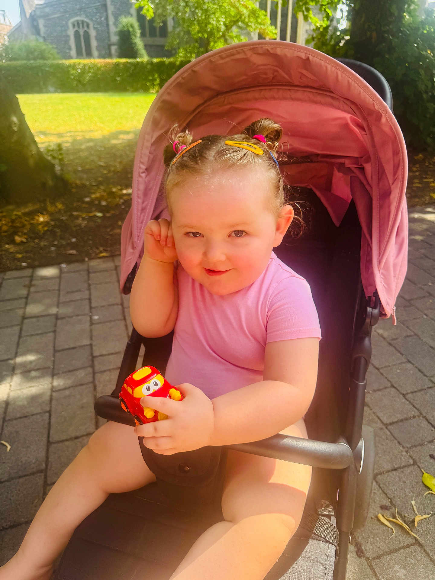 Aaliyah joined the competition — help win amazing prizes! toddler, child, stroller, toy_car, outdoor, park, sunlight, hair_clips, pink_clothing, pavement, greenery, trees, smiling, cute, playful, baby, summer, daylight, person, seat