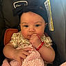 Kalia is registered to the contest to win money with this photo: baby, infant, car_seat, headband, bow, blanket, pink, red_bracelet, floral_clothing, hand, face, eyes, cute, child, person, indoors, comfort, soft_texture, warning_label, closeup