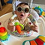 Aiden is registered to the contest to win money with this photo: baby, child, sunglasses, toy, activity_center, carrot_toy, indoor, playtime, cute, surprised_expression, colorful, infant, clothing, plastic_toy, seat, home, person, fun, early_childhood, happy