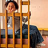 Nour participe au concours pour gagner de l'argent avec cette photo : child, smiling, curly_hair, striped_shirt, jeans, sneakers, chair, wooden_bars, indoor, window, bench, floor, playful, happy, casual_clothing, person, portrait, seated, natural_light, cozy