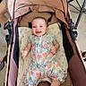 baby, smiling, stroller, floral_outfit, socks, child, indoor, carpet, pillow, seated, blue_chair, happy, person, infant, home, fabric, toy_stroller, light, candid, relaxed