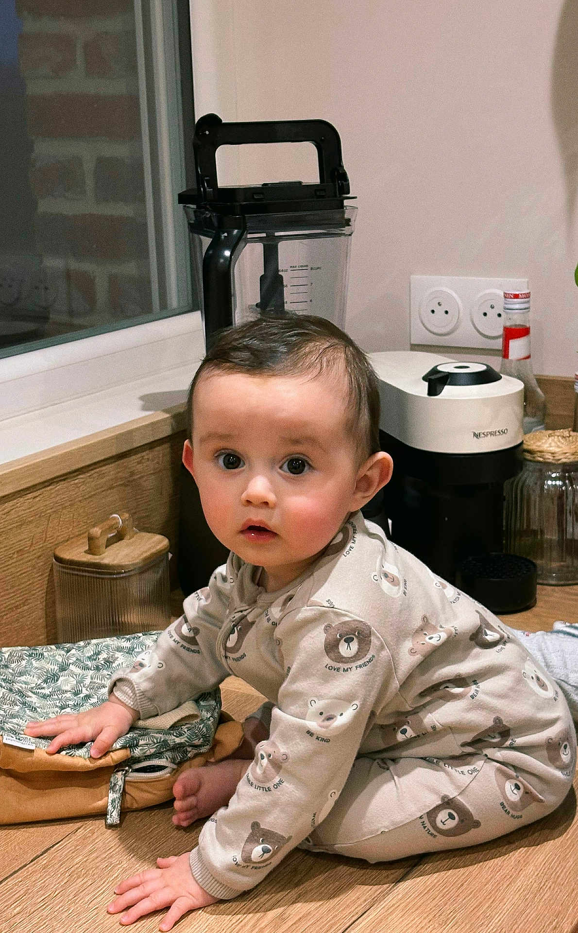 Emilio participe au concours pour gagner de l'argent avec cette photo : child, toddler, baby, pajamas, bear_prints, kitchen, countertop, coffee_machine, nespresso, blender, hardwood_floor, window, jar, bottle, outlet, curious, crawling, hand, face, big_eyes