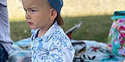 Côme participe au concours pour gagner de l'argent avec cette photo : child, toddler, boy, blue_cap, floral_shirt, pink_shorts, outdoor, picnic_blanket, grass, summer, daylight, face, legs, knees, skin, expression, nature, casual, sitting, portrait