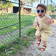 Côme participe au concours pour gagner de l'argent avec cette photo : child, jumping, sunglasses, cap, outdoor, dirt_path, fence, grass, summer_clothing, sandals, expression, daylight, nature, casual_wear, motion, young, person, fun, active, sunny