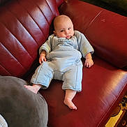 Silas joined the competition — help win amazing prizes! baby, infant, sleepsuit, blue_clothing, red_couch, leather_furniture, cushion, indoor, carpet, foot, hand, person, portrait, relaxing, seated, home_interior, soft_lighting, child, cute, cozy