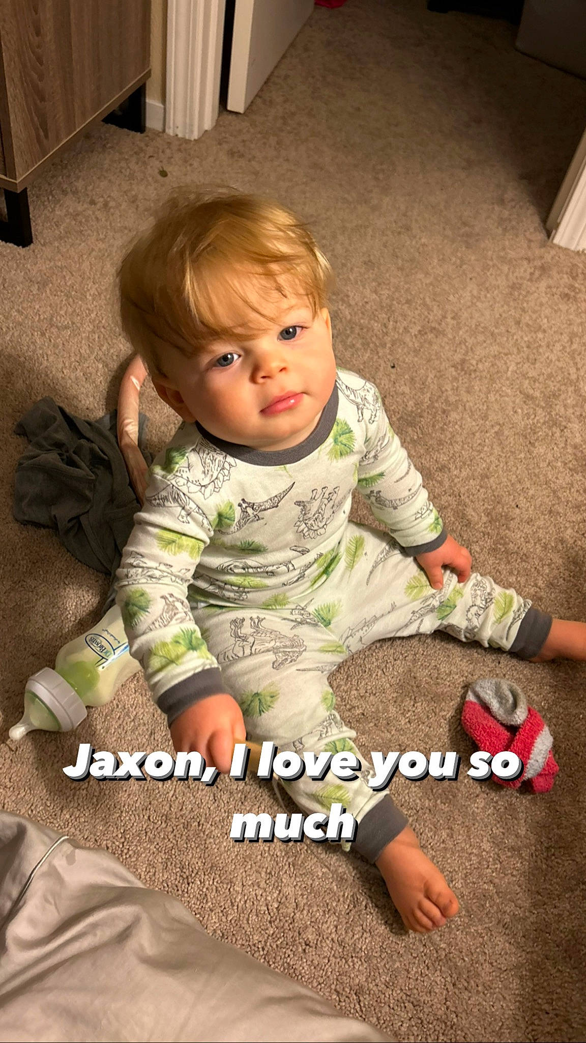 Jaxon is registered to the contest to win money with this photo: baby, baby_toddler_clothing, cheek, child, comfort, facial_expression, floor, flooring, fun, grass, happy, human_leg, mammal, pattern, person, play, sitting, sleeve, t_shirt, toddler