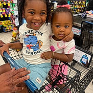 Khadija is registered to the contest to win money with this photo: background, bracelet, braids, child, children, cute, footwear, grocery_store, happy, person, pink_bow, retail, shopping, shopping_cart, shorts, smiling, snacks, store_aisle, supermarket, tshirt
