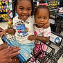 background, bracelet, braids, child, children, cute, footwear, grocery_store, happy, person, pink_bow, retail, shopping, shopping_cart, shorts, smiling, snacks, store_aisle, supermarket, tshirt