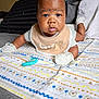 baby, infant, blanket, pacifier, bed, pillow, mittens, bib, face, expression, indoor, child, cute, lying_down, patterned_blanket, clothing, skin, head, eyes, mouth
