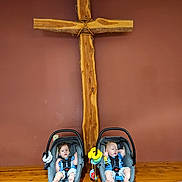 Zane And Rayden is registered to the contest to win money with this photo: toddler, baby, car_seat, child, wooden_cross, wall, floor, brick, toy, infant, seatbelt, indoor, person, two_children, blue_clothing, wood, decor, cute, sitting, expression
