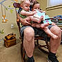 man, child, toddler, rocking_chair, book, reading, indoor, carpet, wall_decals, fox, window, shelf, books, toy, shorts, socks, shoes, family, parenting, nursery