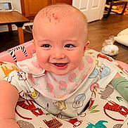 Rex is registered to the contest to win money with this photo: baby, infant, smiling, bib, strawberry_pattern, activity_seat, animal_print, elephant, tiger, wood_floor, door, chair, diaper, face, head, eyes, cheek, happy, clothing, playmat