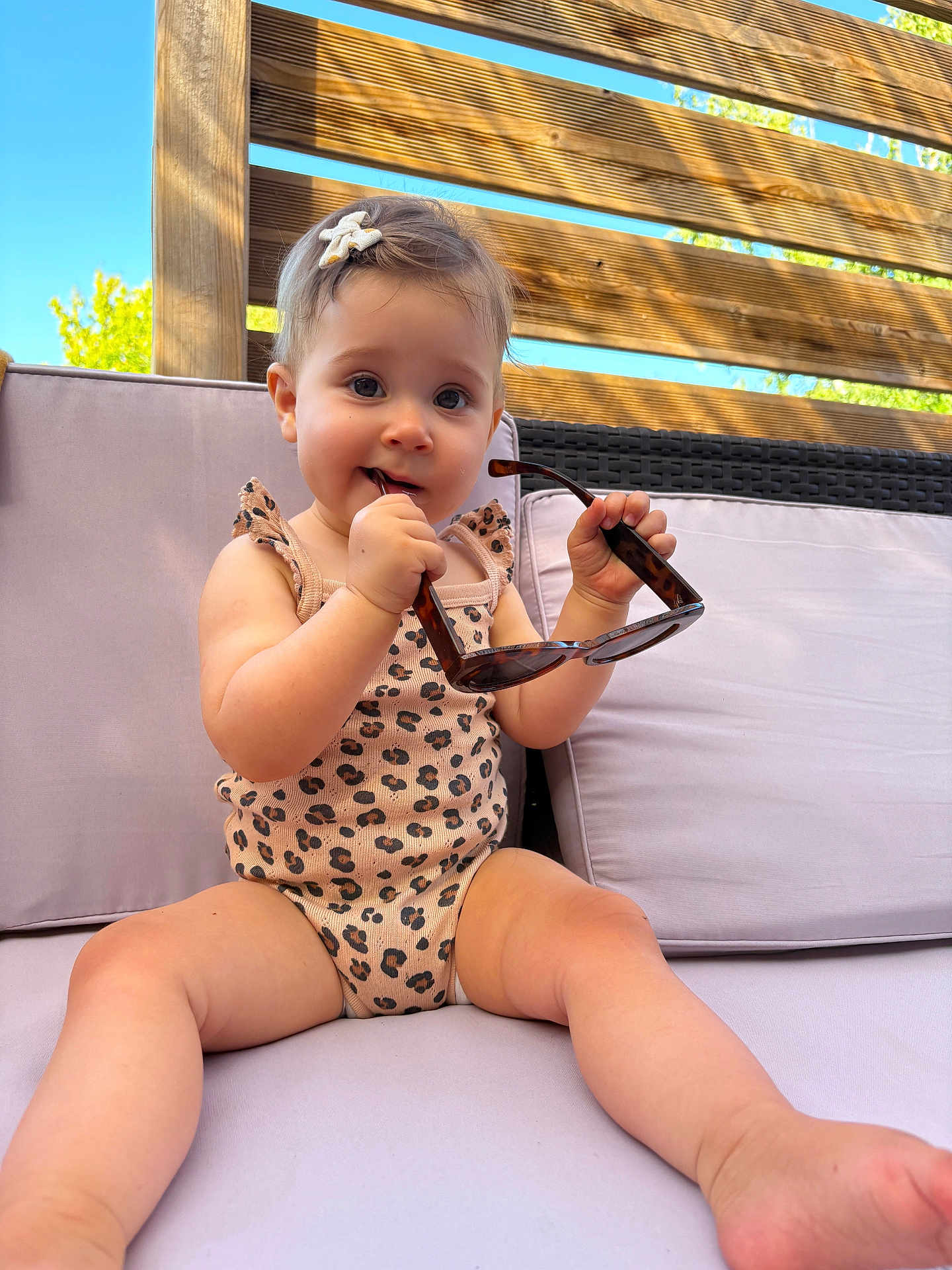 Charlie a rejoint le concours — aidez-le/la à gagner de superbes lots ! toddler, child, sunglasses, outdoor, sofa, cushion, wooden_fence, blue_sky, summer, cute, playful, infant, clothing, leopard_print, hair_clip, barefoot, smiling, sunlight, relaxing, portrait