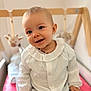 baby, child, smiling, white_blouse, denim_pants, crib, soft_toys, giraffe_toy, elephant_toy, blue_eyes, happy, portrait, indoor, cute, infant, hand_holding, seated, person, clothing, cozy