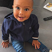 Simao a rejoint le concours — aidez-le/la à gagner de superbes lots ! book, casual, child, clothing, cute, face, floor, happy, hoodie, indoor, jeans, large_eyes, person, playful, shoes, sitting, smiling, tile_floor, toddler, toy